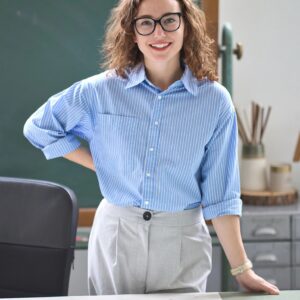 Young happy woman teacher coach standing at desk in classroom office. Portrait
